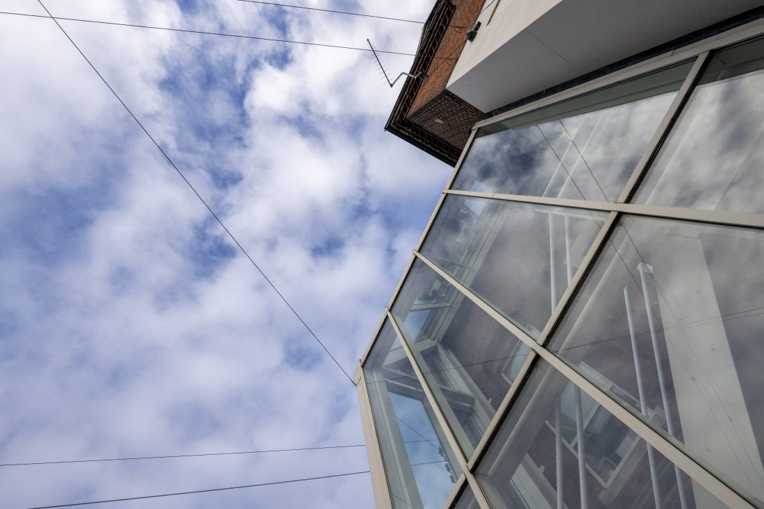 Commercial building with glass panes from ground level, looking up towards blue sky and clouds