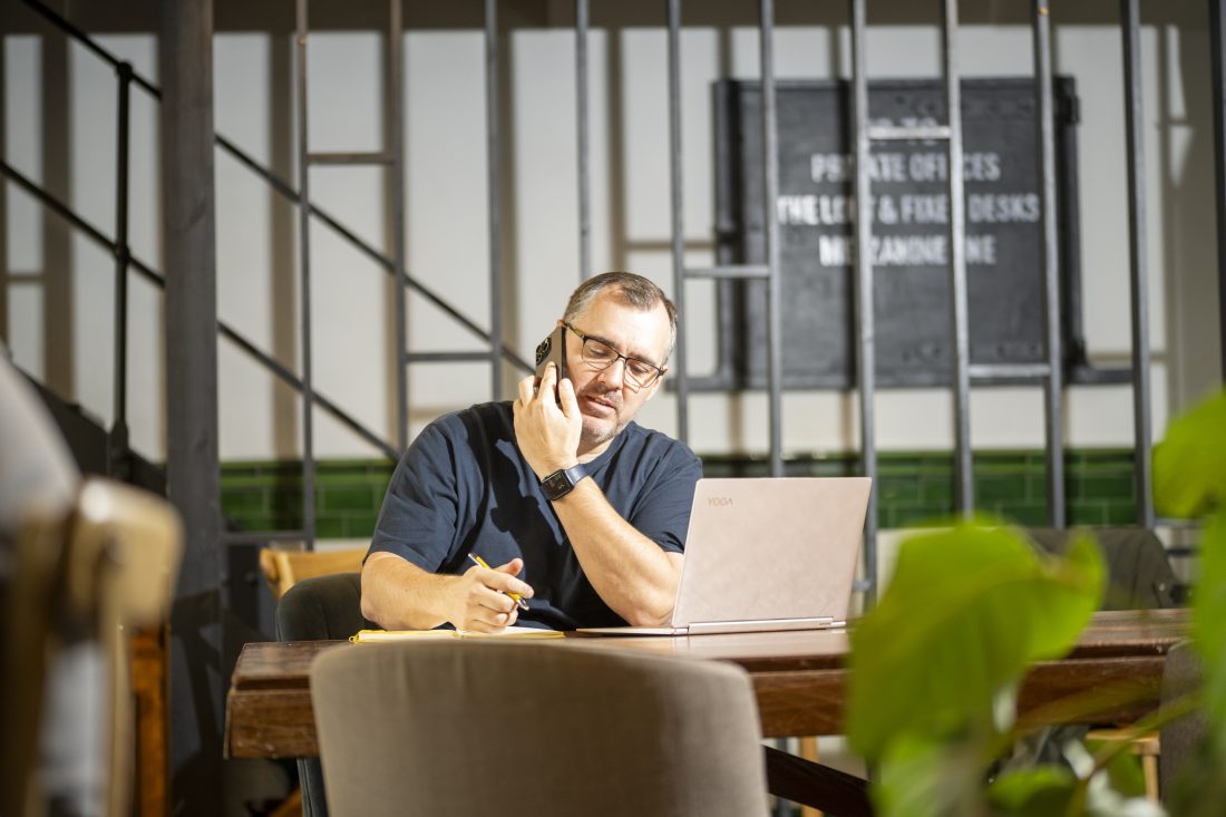 Chartered building surveyor on a phone call concentrating, inside rustic office setting with staircase in background and plant in foreground