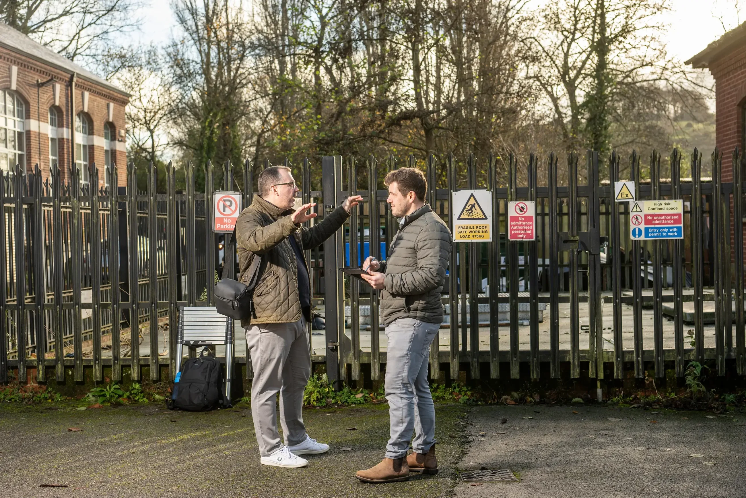 Two chartered building surveyor outside a commercial premises, railings in the background and view down a street