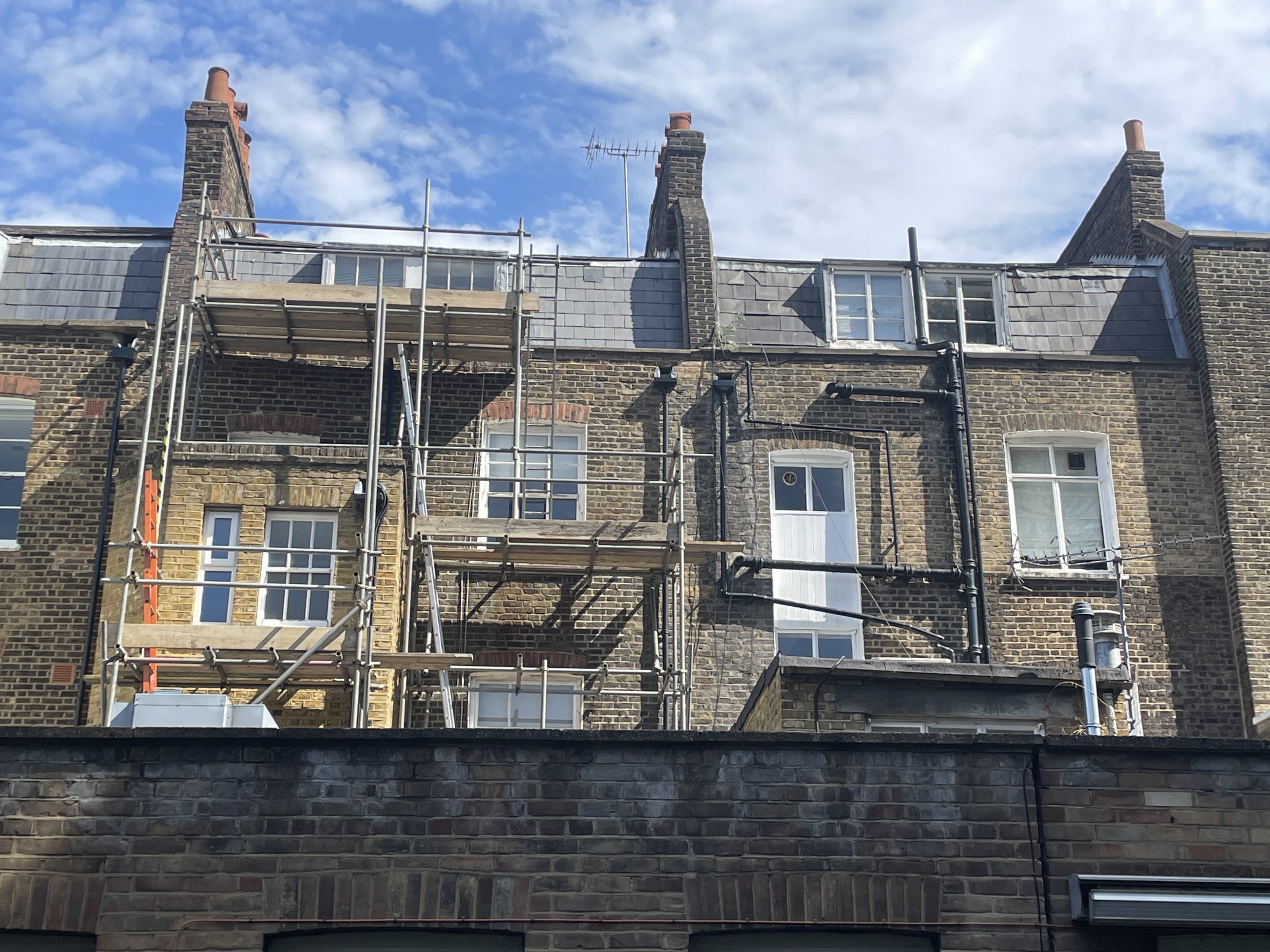Rear view of London rental property surrounded by scaffolding with blue sky and clouds