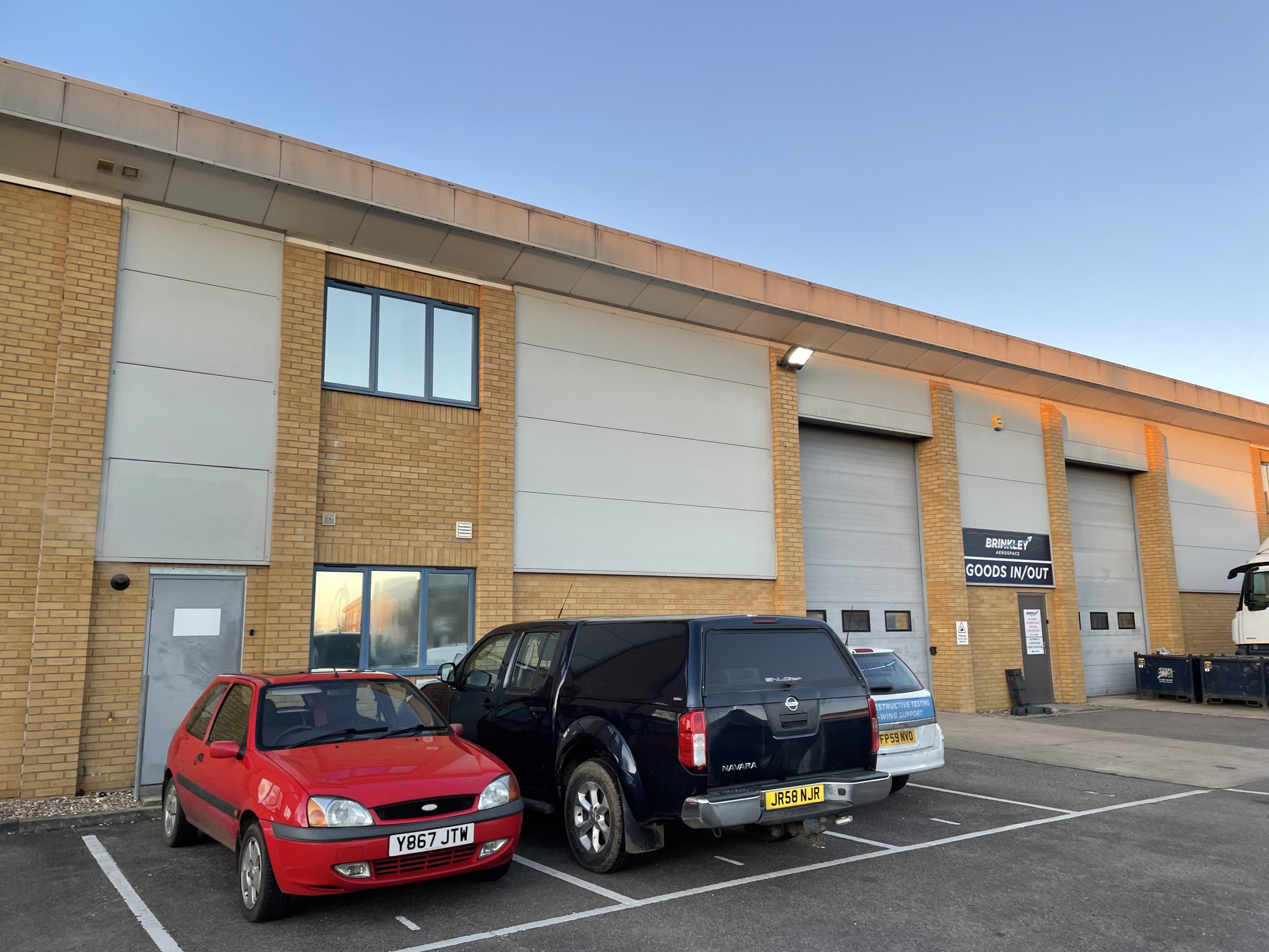 Large industrial warehouse consisting of multiple units, all with roller doors and parking spaces out the front